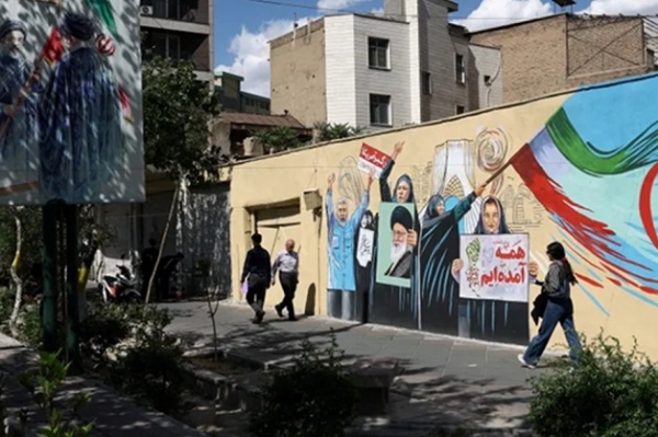 یہ ایران کا دارالحکومت تہران ہے۔ سڑک کے کنارے آنجہانی سپریم لیڈر آیت اللہ علی خامنہ ای کا ایک میورل (دیواری تصویر) بنا ہوا ہے۔ لوگ وہاں سے گزر رہے ہیں۔ فوٹو انٹرنیٹ میڈیا